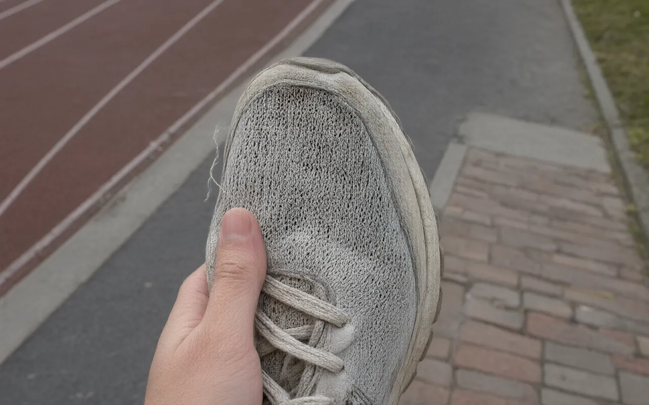 A worn mesh upper on a running shoe held against a window
